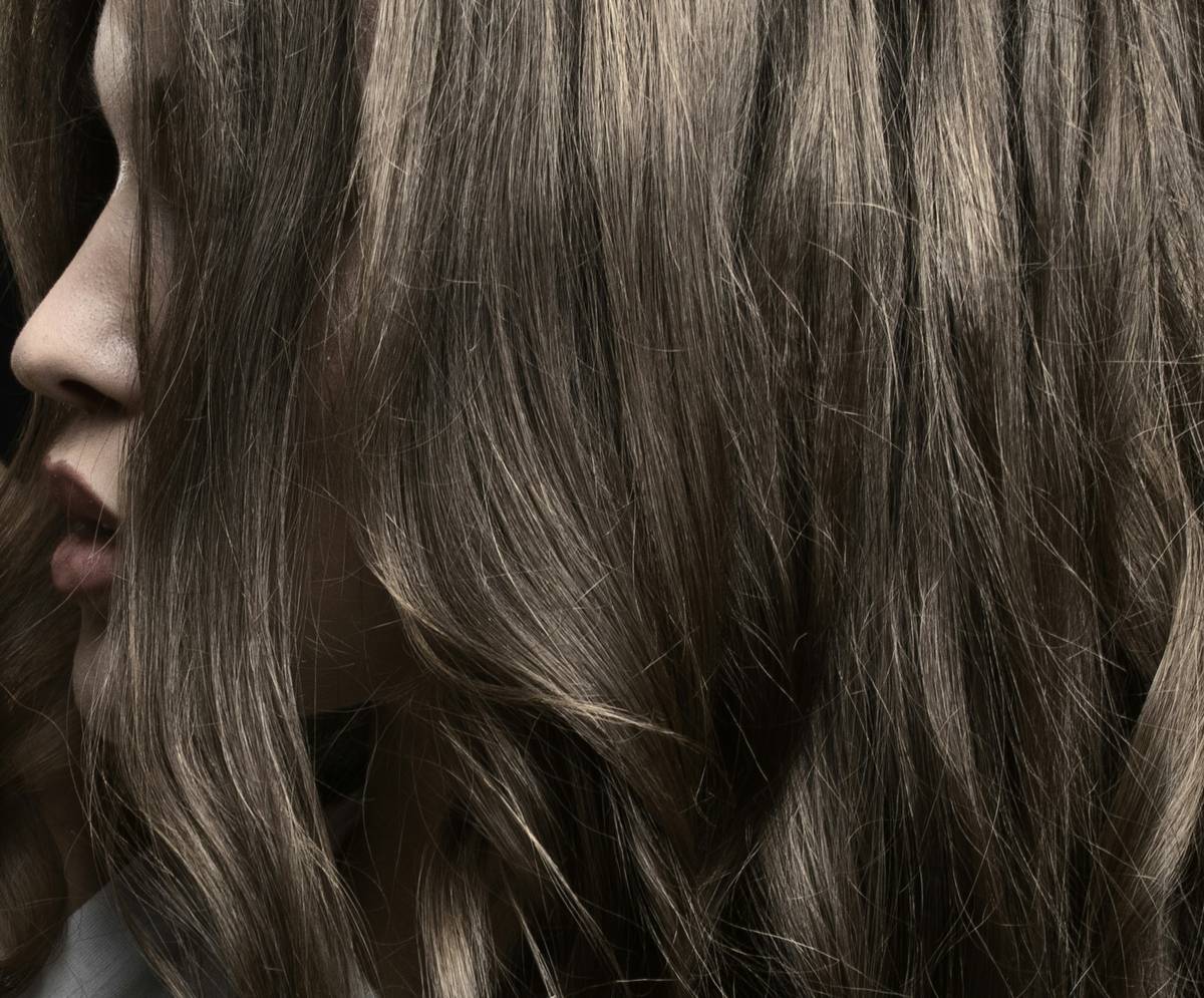 Close-up of woman applying hair shine product to damp strands for natural gloss